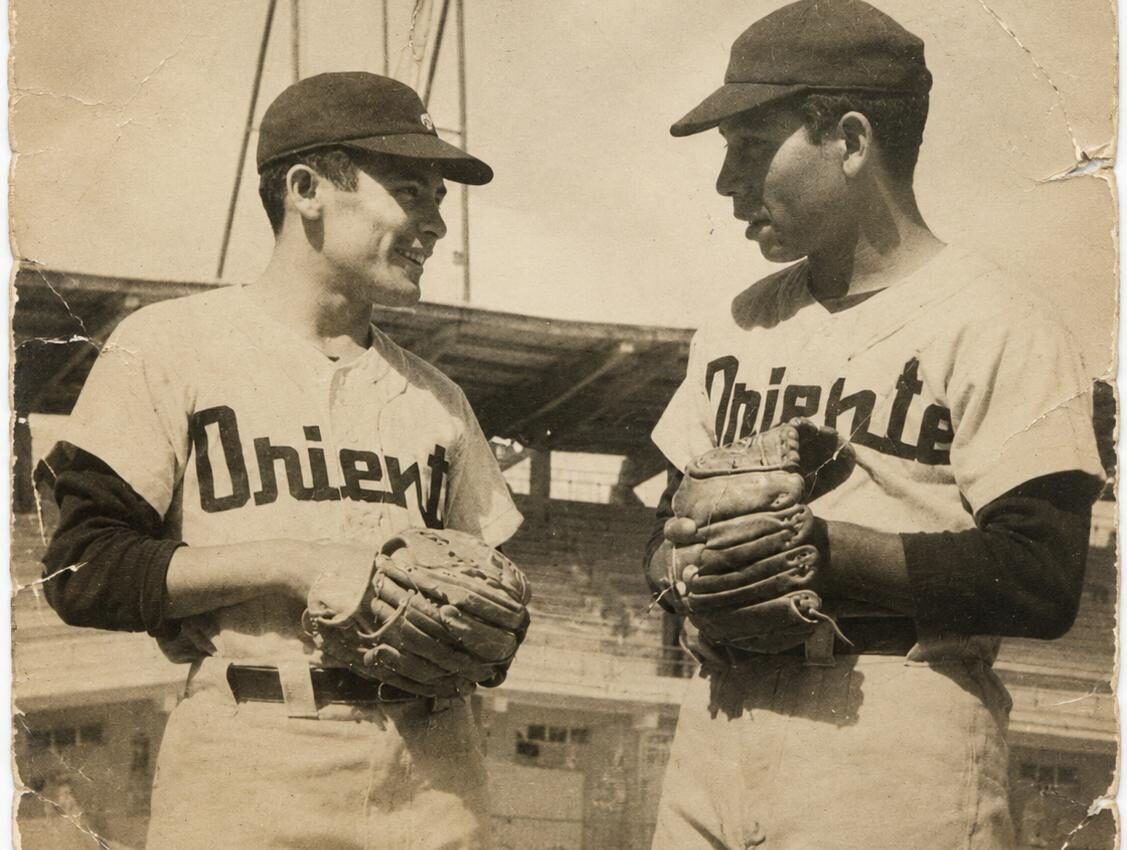 Dos peloteros con guantes ante la torre de luces del estadio