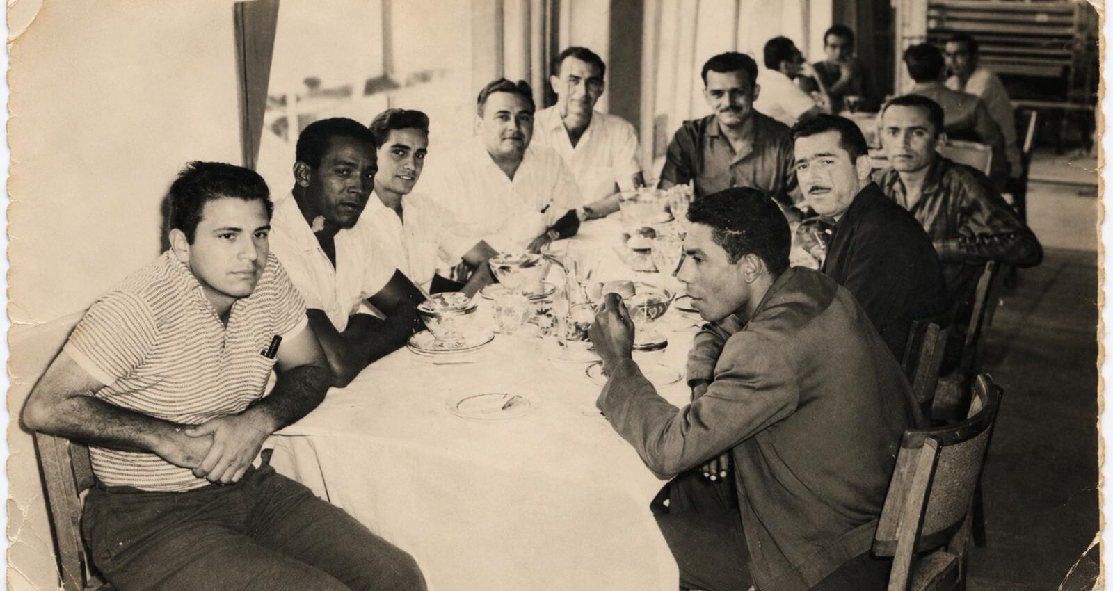 Una decena de hombres sentados a una mesa larga con mantel blanco