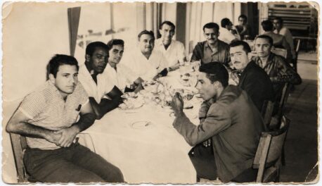 Una decena de hombres sentados a una mesa larga con mantel blanco