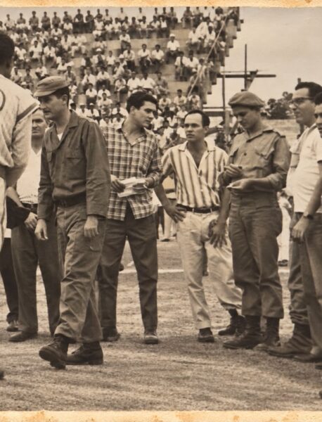 Un pelotero con el número 30, de espaldas, ante una fila de hombres de civil y de uniforme militar