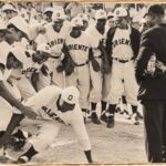 Peloteros con el uniforme de Oriente ríen alrededor de un compañero agachado